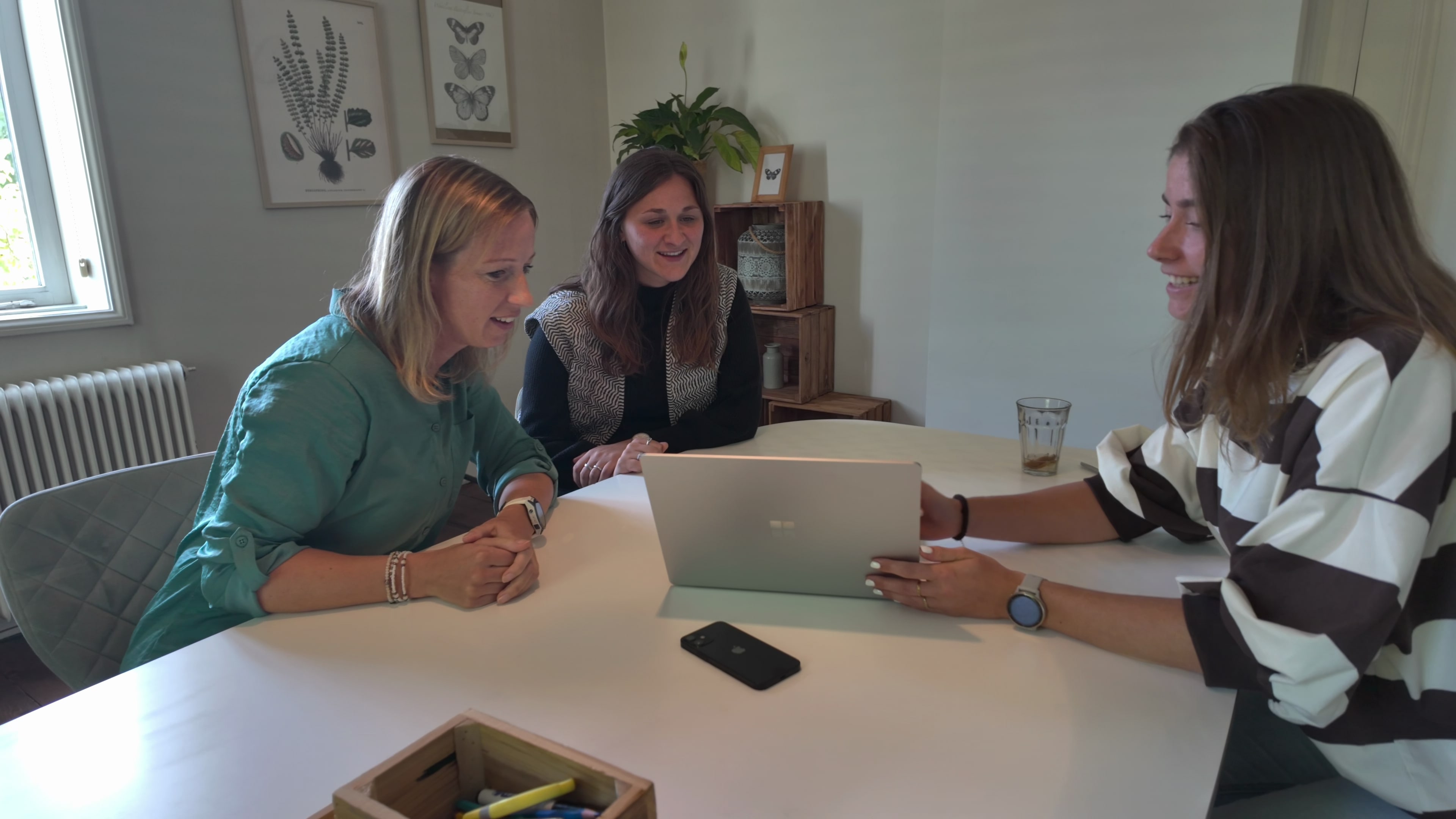 Drie collega’s bij Kind & meer bekijken samen een laptop, met een telefoon op tafel